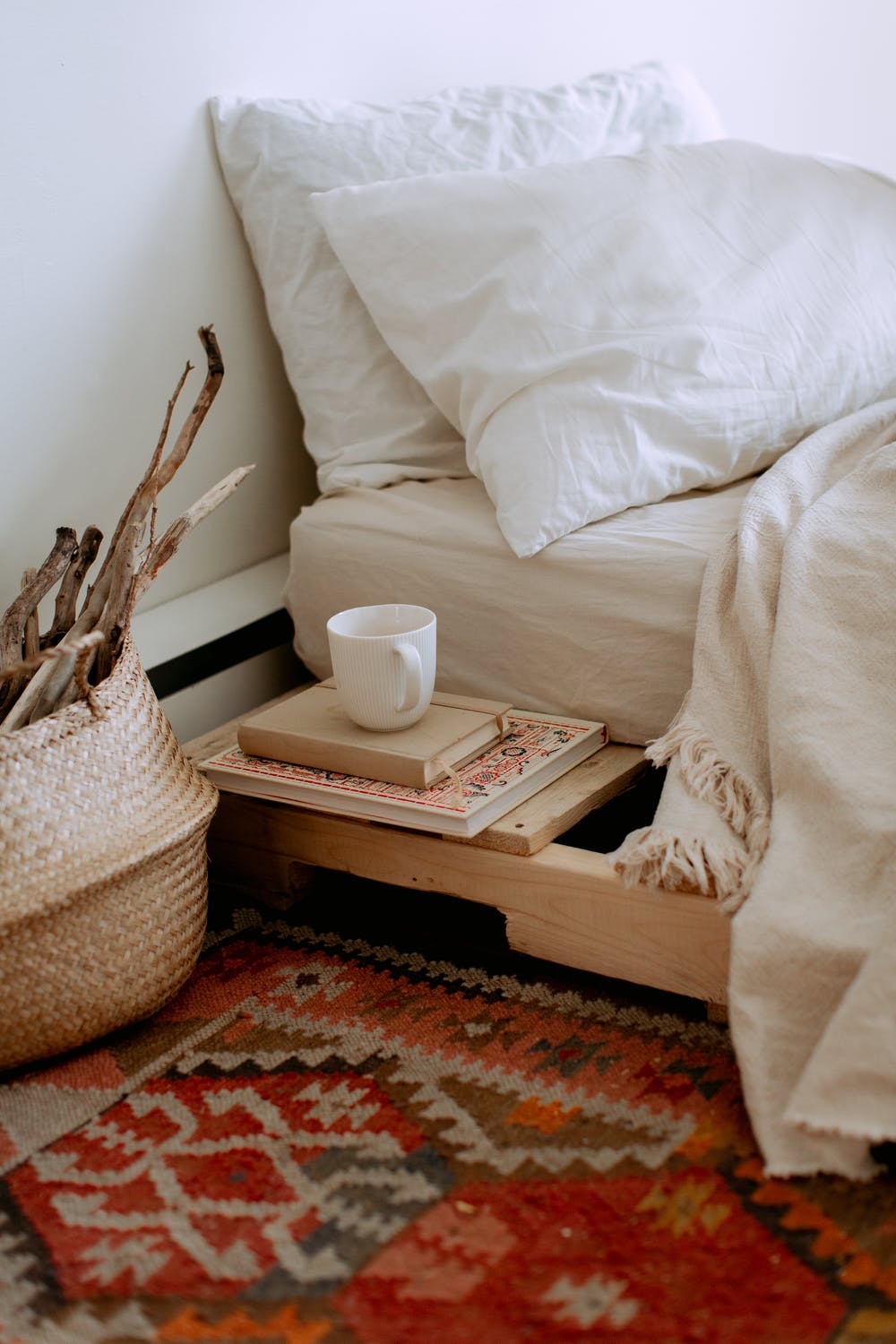 Beautiful kilim of red, orange, and brown beside a bed and woven basket.