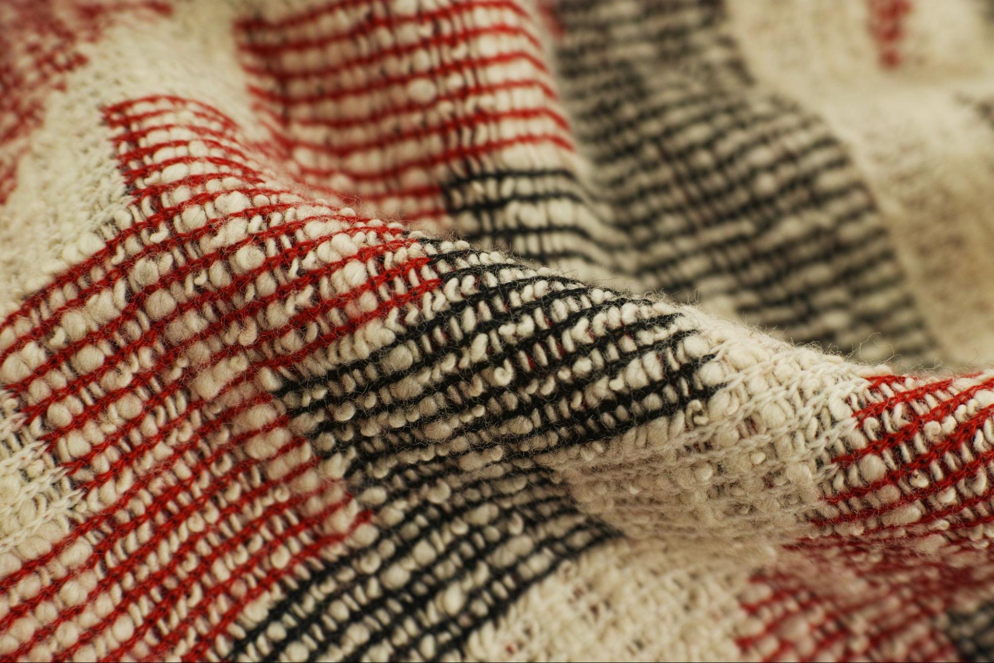 Closeup of natural fibers in a rug that is red, black, and cream colored.