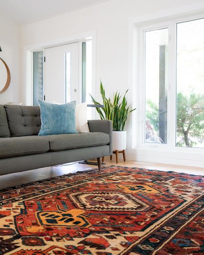 Antique rug on the floor of a living room with a modern, grey couch and French doors.