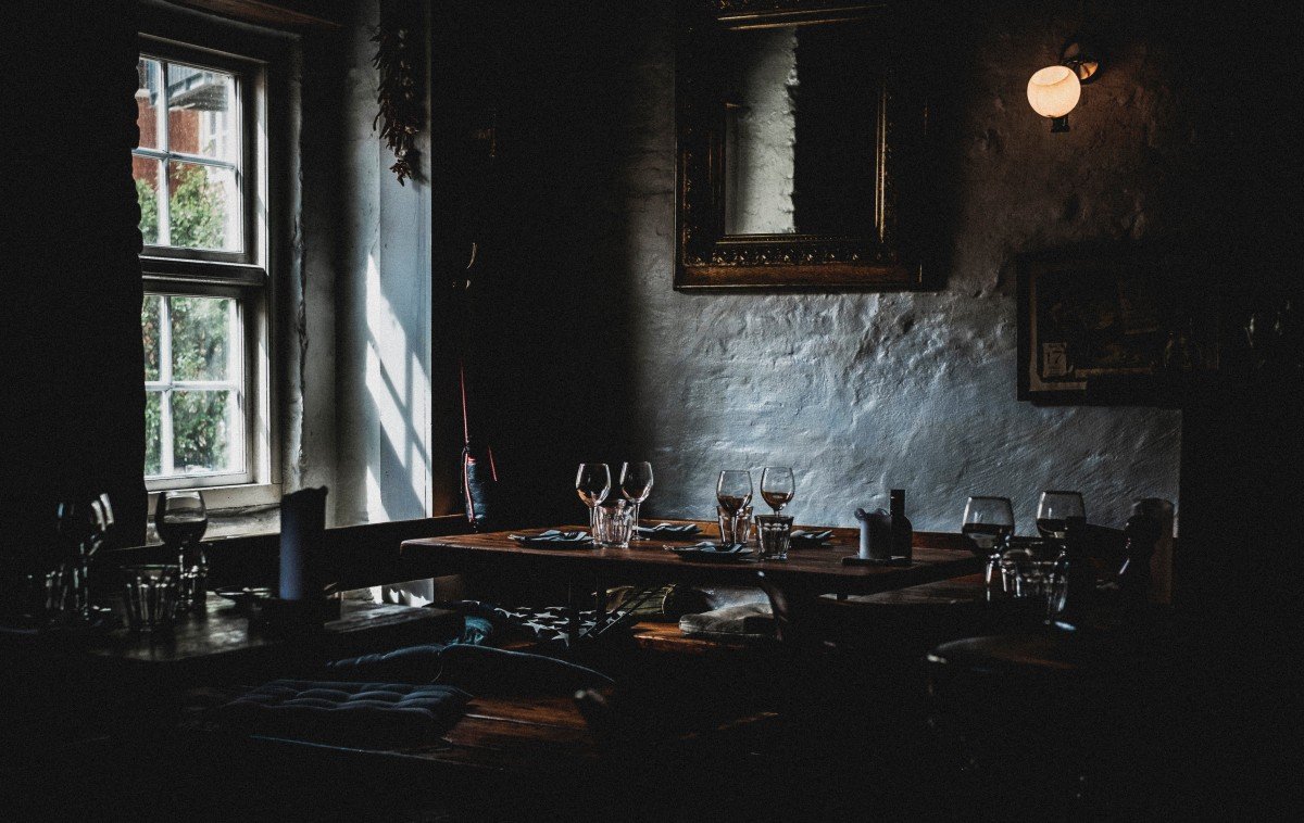Dark dining room with modern gothic details: lights and shadows, wall sconces, mirrors, and antique wooden furniture.