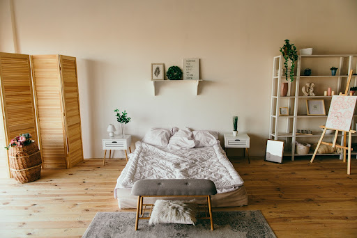 A small rug beneath a bench at the foot of a bed in a serene bedroom with plants and an art easel.