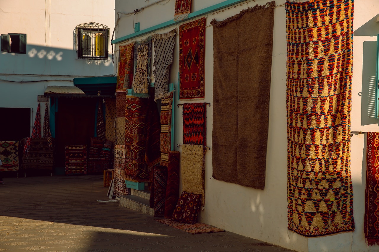 Beautiful handmade rugs and tapestries hung up to showcase their patterns and weave in an outdoor market.