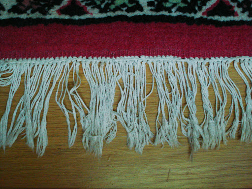 Closeup of white fringe along the edge of a red Persian rug.