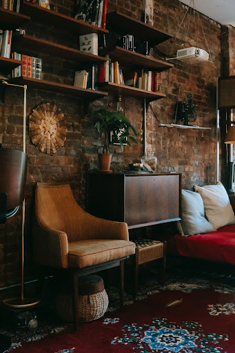 A beautifully decorated bedroom with exposed brick, bookshelves, and a deep red persian carpet on the floor.